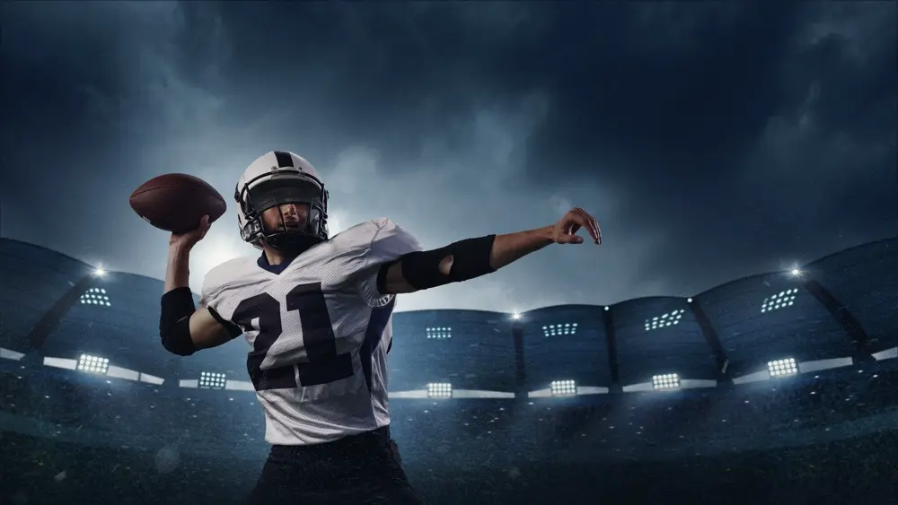 Jogador de futebol americano lançando a bola em estádio iluminado durante a noite, simbolizando a temporada da NFL 2025.
