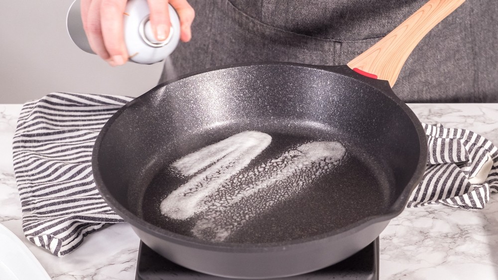 Pessoa aplicando óleo em frigideira antiaderente durante o processo de cura para proteger o revestimento e aumentar a durabilidade da panela.