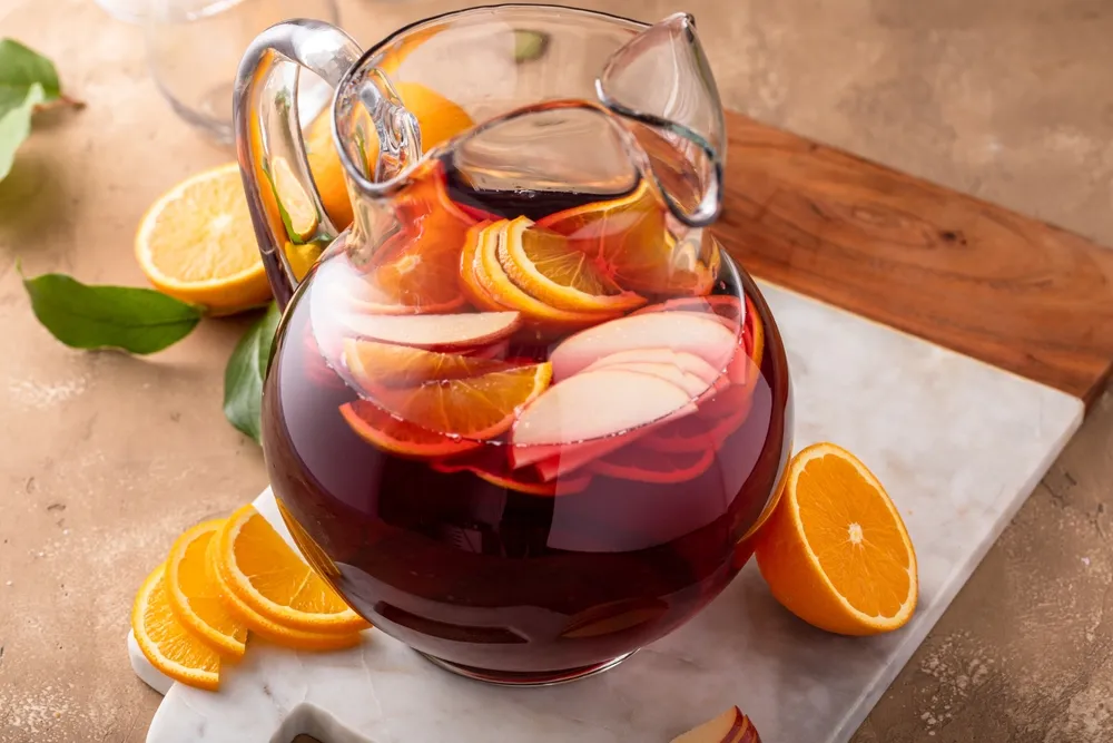 Jarra de sangria tradicional com vinho tinto, fatias de laranja e maçã fresca, bebida refrescante e frutada servida sobre mesa rústica.