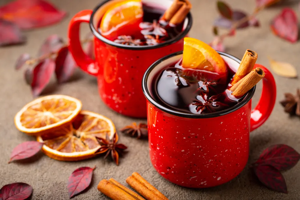 Canecas vermelhas com quentão sem álcool decorado com laranja, canela e anis-estrelado, bebida quente tradicional servida em clima de outono.