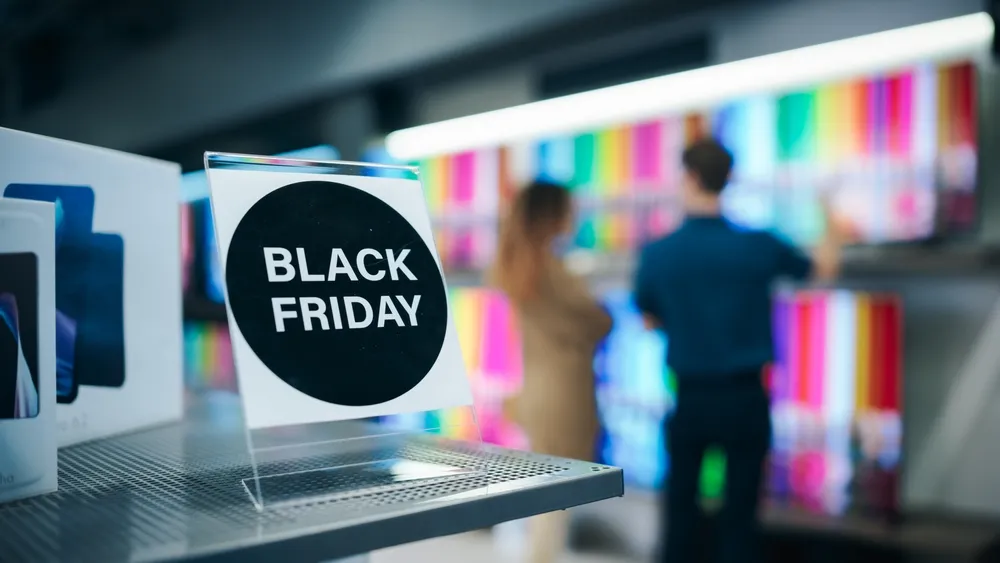 Pessoa escolhendo Smart TV em loja durante a Black Friday 2025, com sinalização de promoções e ofertas especiais de televisores Philco.