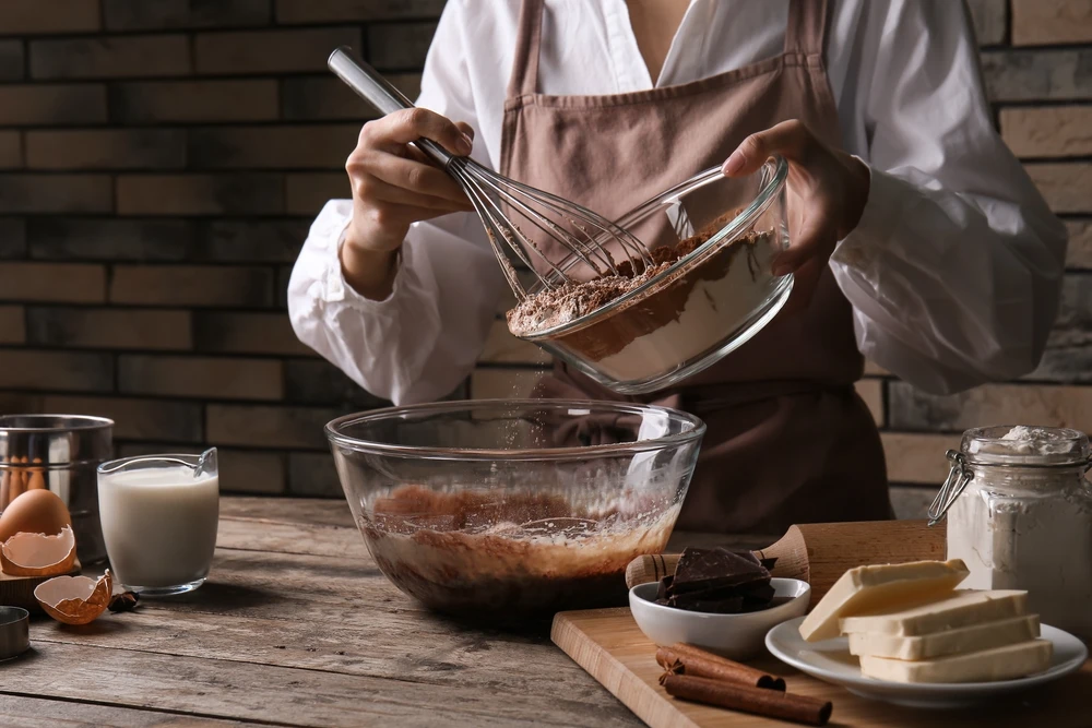 Mulher preparando massa de chocolate na mesa da cozinha, close-up